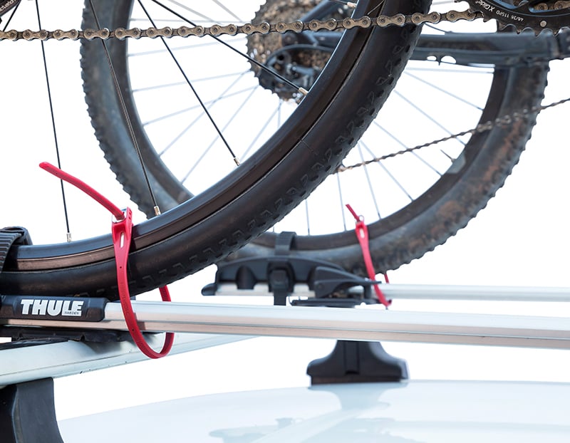 rear wheels of two bicycles attached to a roof rack on the roof of a car with z loks locking wheels to the rack