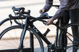 Women locking road bike in a town with the DX D lock and the frame mount is mounted to the downtube of a roadbike
