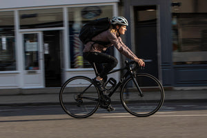 Women riding through a village commuting with a rucksack on and the DX Frame mounted bike lock attached to her road bike