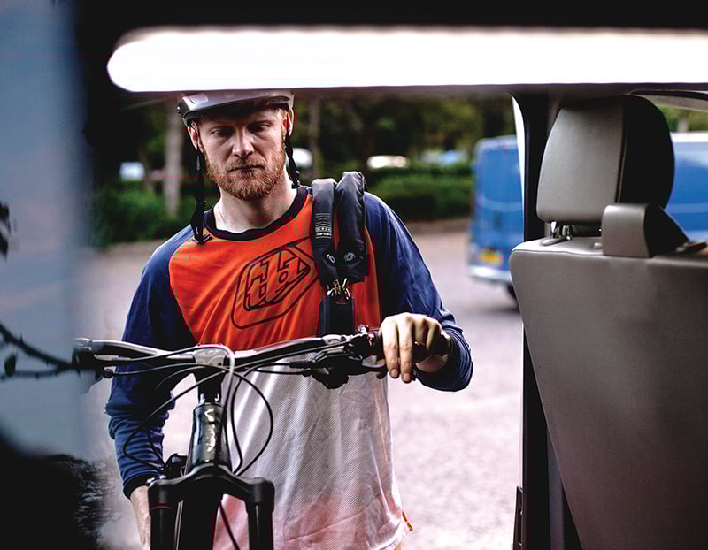 man putting mountain bike into van with a heavy duty chain lock slug over his shoulder