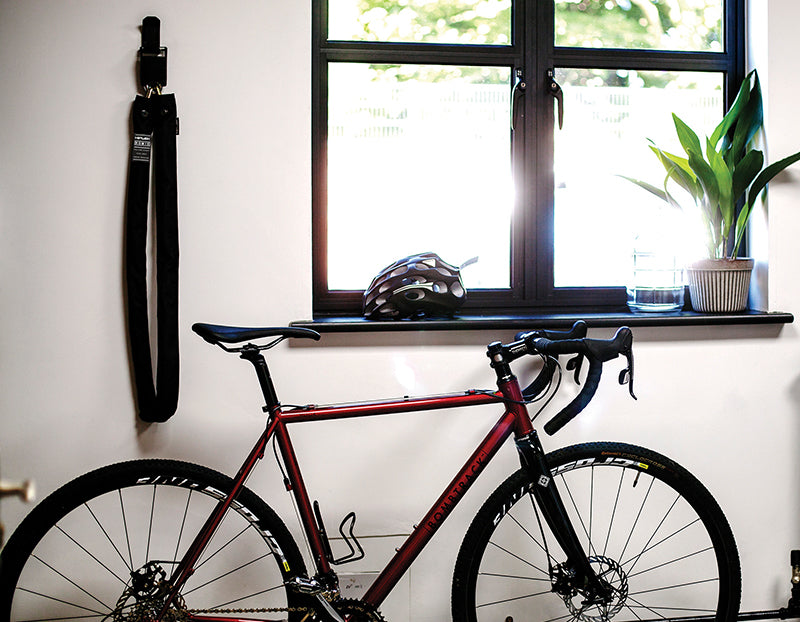 bike in a house lent against a wall with a long heavy duty chain lock hooked to the wall
